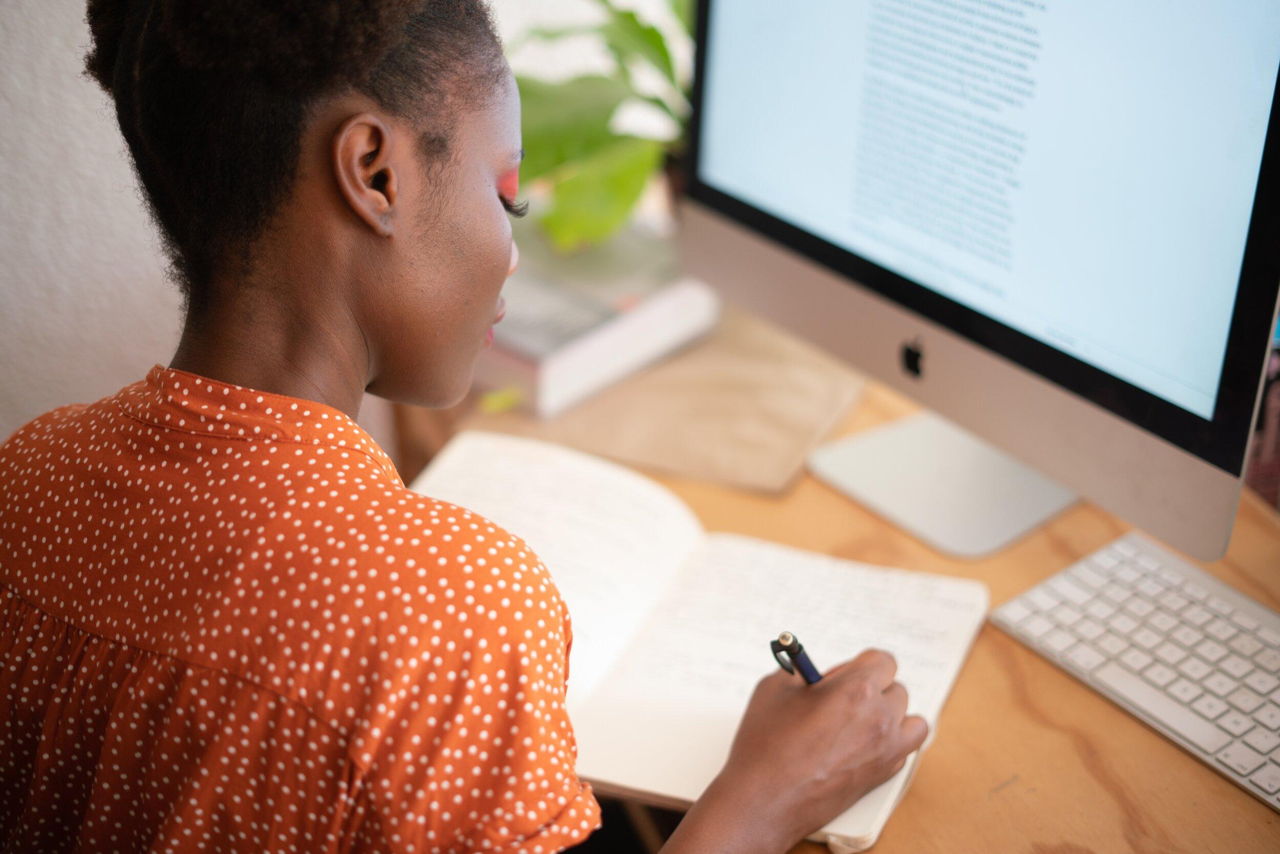 A woman writes in a notebook at her desk.